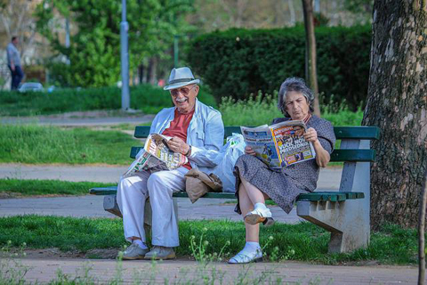Rentner Ehepaar sitzt auf einer Bank im Park und liest Zeitung, Altersvorsorge